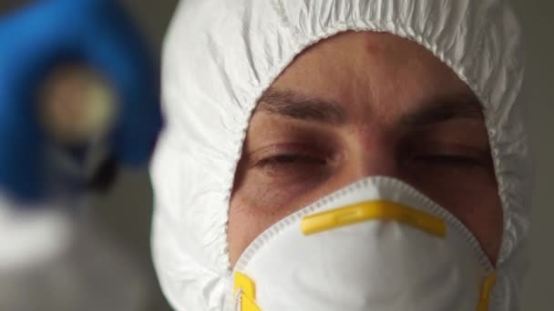 Close-up portret van een man in een beschermend pak, masker, handschoenen en bril schijnt een zaklamp. Grensgeneeskundig onderzoek, coronaviruspandemie — Stockvideo