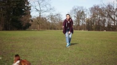 Yavru köpeğiyle bahar parkında yürüyüş yapan güzel bir genç kadın. Köpek neşeyle bir sopayla oynar. Mutlu aile hafta sonu