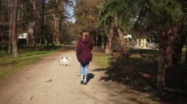 Sırtında sırt çantası olan güzel bir kız bahar parkında köpeğini tasmayla gezdirir. Köpek yürüyüşü, köy hayatı, hayvan bakımı, mutlu hafta sonları.