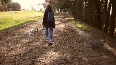 Genç bir kadın, köpeğiyle bir bahar parkında bir patika boyunca koşuyor. Kız bordo bir ceket giymiş ve sırtında bir sırt çantası var. Bahar tatili