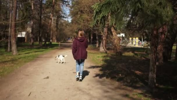 Belle fille avec un sac à dos sur le dos promène son chien en laisse dans le parc du printemps. Promenade en chien, vie de village, soins aux animaux, week-end heureux 