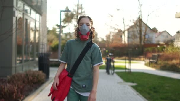 A fiú a lélegeztetőgépben, piros táskával sétál az utcán. Karantén az európai országokban. Coronavirus-járvány. COVID-19. Arcmaszkot viselő gyermek — Stock videók