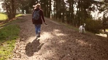 Genç bir kadın köpeğiyle parkta bir yol boyunca yürüyor. Karatentin sırasında bir köpekle yürüyüşe çıkmak. Mutlu aile hafta sonları. Arka plan