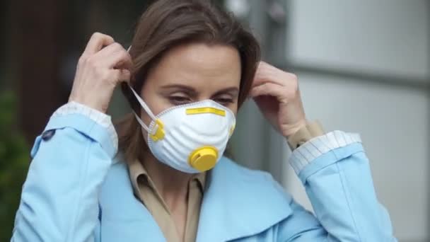 En vacker kvinna tar på sig en skyddande mask. Skydd mot coronovirus covid-19. Porträtt utomhus under karantänen — Stockvideo