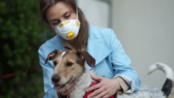 Ung kvinna med medicinsk ansiktsmask sittandes tillsammans med sin hund. Coronavirus koncept, covid-19 — Stockvideo