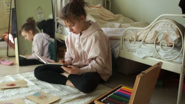 Colegiala dibuja dibujos en una caja de bocetos con lápices de colores. Muestra su dibujo y sonrisas. pasatiempos de autoaislamiento y cuarentena — Vídeos de Stock