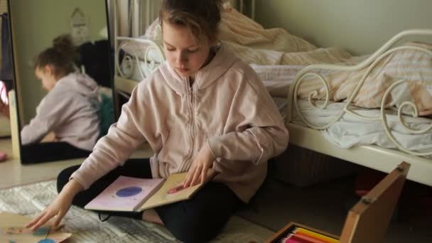 Школьница в своей комнате открывает большую коробку с цветными карандашами и открывает свой эскиз рисунками. Искусство во время карантина, развлечения для детей в отпуске, счастливое детство — стоковое видео
