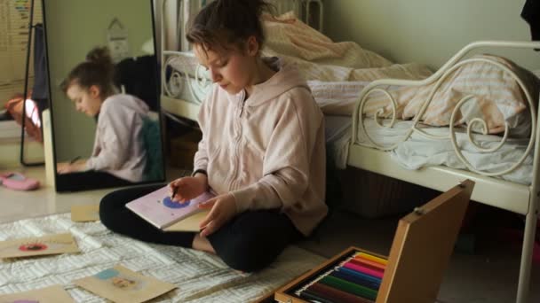 Hermosa chica dibuja con lápices de colores mientras está sentada en el suelo en su habitación. Adolescente feliz durante la cuarentena y el autoaislamiento. Creatividad infantil — Vídeo de stock