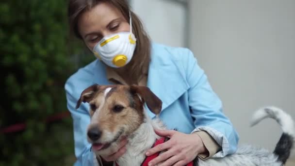 Jovem mulher em uma máscara protetora abraça seu cão de estimação. Quarentena durante a epidemia de coronovírus, covid 2019. Cuidados com animais — Vídeo de Stock