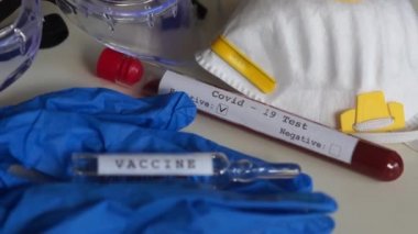 Masanın üzerinde, üzerinde kan plazması örneği olan bir test tüpü var. Coronovirüs covid-19 testi pozitif çıkmış. Koruyucu tıbbi maske ve gözlük, mavi tıbbi eldiven.