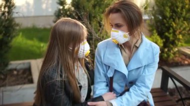 Anne ve kızı koruyucu maskeli bir kız çocuğu şehir parkında bir bankta oturup sarılıyor. Karantina yürüyüşü, koronovirüs salgını, covid-19.