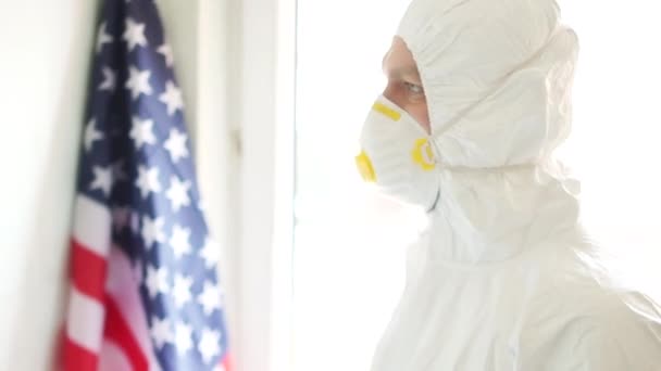 Americký lékař v ochranném obleku si nasadí masku na pozadí americké národní vlajky. Muž odchází léčit lidi. Boční pohled. Coronovirus covid19 in USA — Stock video