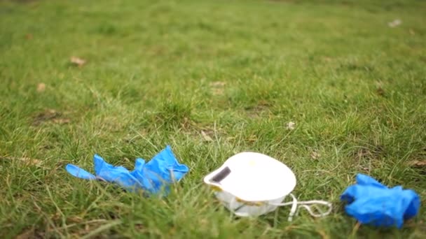 Медицинская маска и перчатки лежат на траве. Эпидемия короновируса ковид-19 и экология. Медицинские отходы. Загрязнение окружающей среды — стоковое видео