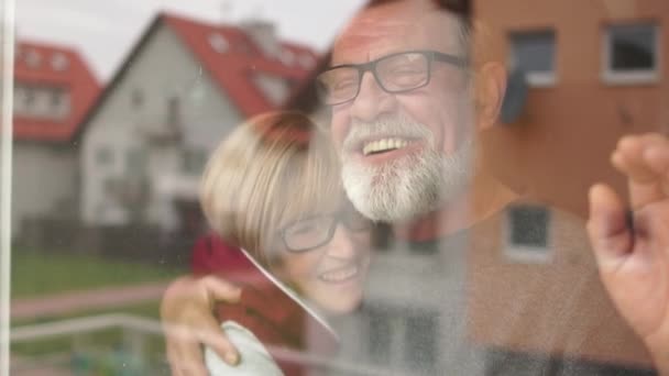 The old lonely family in quarantine looks out the window. Quarantine at home for coronavirus pandemic prevention. A man hugs a woman and they laugh cheerfully, positive attitude — Stock Video