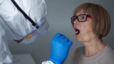 Koruyucu kıyafetli doktor yaşlı bir emeklinin boğazından örnek alıyor. Koronovirüs testi, PCR reaksiyonundan invazif olmayan tanı yöntemi