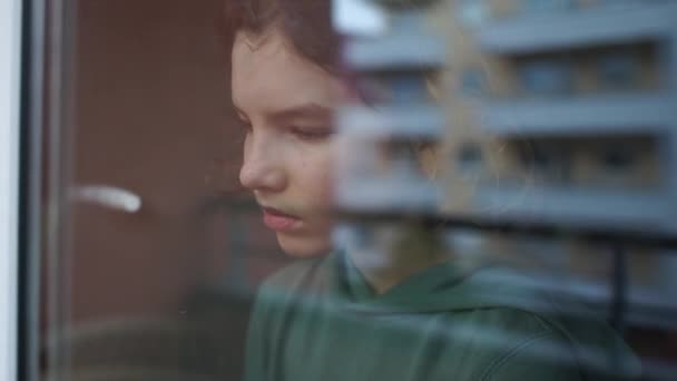 窓の近くに悲しいカーリー少年の少年は、ガラスの上に頭を下げ、自己分離中のうつ病。隔離中の子供たち。検疫コロノウイルス｜Covid-19 — ストック動画