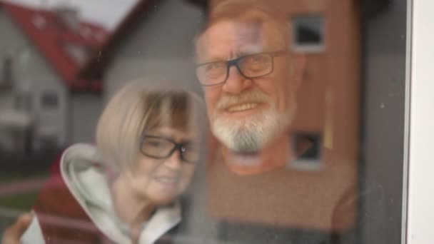 Quarantine at home for coronavirus pandemic prevention. Family of elderly people, husband and wife are standing embracing at the window. Man and woman are smiling — Stock Video