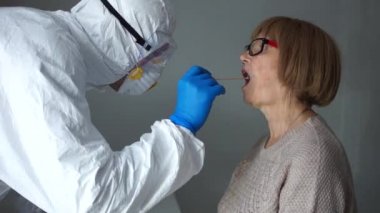 Coronovirüs enfeksiyon testi. Koruyucu giysili bir sıhhiye Coronovirus covid-19 belirtileri gösteren bir kadının boğazından örnek alıyor.