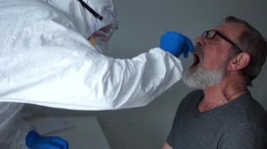 Koruyucu kıyafetli doktor önce yaşlı bir kadın emekliden, sonra da kocasından örnek alıyor. PCR reaksiyonunun zararsız tanı metodu. Coronovirus aile risk grubunu test ediyor
