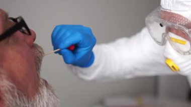Nüfusu koronovirüs enfeksiyonu için test ediyorum. Doktor yaşlı bir hastadan ağız boşluğundan örnek alıyor. Coronovirus Covid-19, risk grubu.