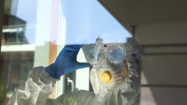 Pencerenin yakınındaki bir hastanede koruyucu giysili yorgun kadın doktor maskesini ve gözlüklerini çıkarıp rahatça nefes alıyor. Salgın Coronovirus Covid-19, virüs SARS-CoV-2