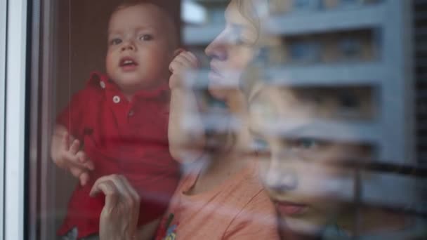 Концепция карантина и самоизоляции. Семья у окна за стеклом, отражение домов в стекле, мать и двое детей грустные. Карантин Короновируса Ковид-19 — стоковое видео