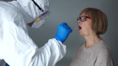Koruyucu kıyafetli doktor Coronovirus covid-19 belirtileri gösteren bir kadının boğazından örnek alıyor. Coronovirüs enfeksiyon testi