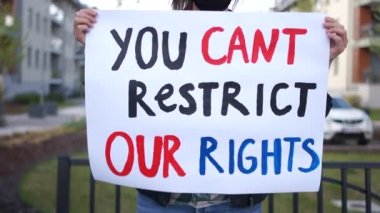 Koronovirüs kovid-19 karantinası sırasında insan haklarının kısıtlanmasına karşı saldırı. Maskeli güzel bir kızın portresi ve üzerinde bizim haklarımızı kısıtlayamayacağınız bir yazı var.