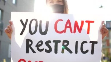 Koronovirüs karantinası sırasında insan haklarının kısıtlanmasına karşı toplu protestolar. Maskeli güzel bir kızın güneşli portresi. Üzerinde haklarımızı kısıtlayamayacağınız bir yazı var.