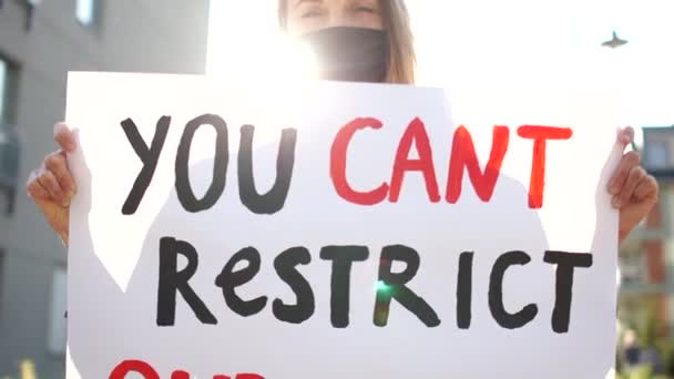 Massale protesten tegen de beperking van de mensenrechten tijdens de quarantaine van het coronovirus. Zonnig portret van een mooi meisje in een masker met een poster met de inscriptie kunt u niet beperken onze rechten — Stockvideo