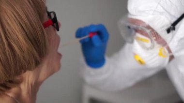 Nüfusu koronovirüs enfeksiyonu için test ediyorum. Doktor yaşlı bir hastadan ağız boşluğundan örnek alıyor. Coronovirus Covid-19, risk grubu.