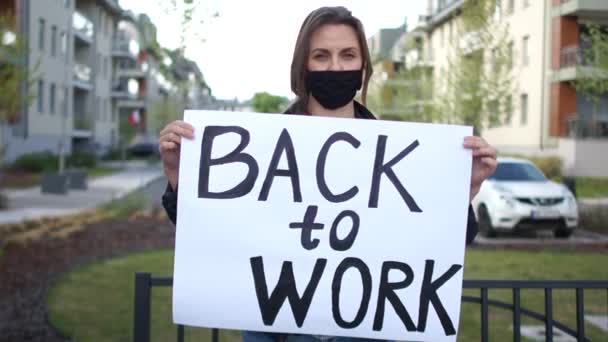 Fille activiste avec une affiche de retour au travail dans les mains. Femme porte un masque de protection noir, protestation pendant la quarantaine du coronovirus covid-19 — Video