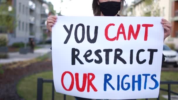 Chica activista con un cartel que no puede restringir nuestros derechos en las manos. Mujer lleva máscara protectora negra, protesta durante cuarentena de coronovirus covid-19 — Vídeo de stock