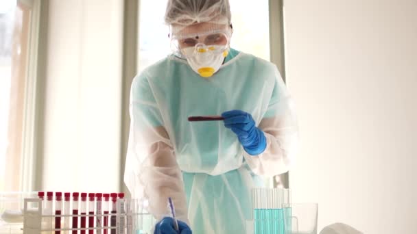 Лаборатория забирает пробирку с образцом крови зараженного Ковида-19. Сотрудник лаборатории фиксирует результаты тестов на короновирус ковид-19 сарс-ков-2 — стоковое видео