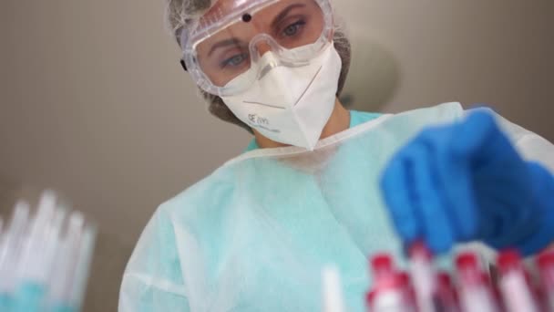 Diagnósticos Sars-CoV-2. Hermosa asistente de laboratorio en el laboratorio sostiene un tubo de ensayo con una muestra de sangre infectada con coronovirus Covid-19 — Vídeos de Stock