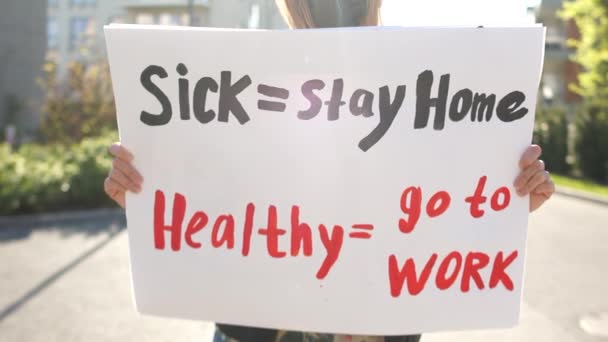 Nemocný - zůstaň doma zdravý - jdi do práce. Slunečný portrét maskované dívky s plakátem proti uzamčení karanténních omezení — Stock video