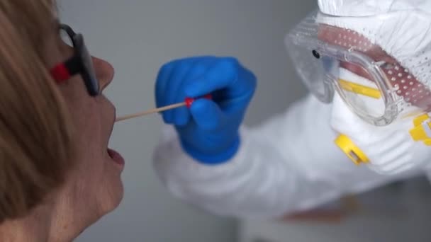 Coronovirus test, test de détermination de l'infection par le coronovirus. Gros plan Un microbiologiste en combinaison de protection prélève un échantillon de biomatériau dans la cavité buccale d'une femme âgée — Video