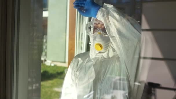 流行性结肠炎病毒covid-19，医疗崩溃。身穿防护服的疲倦的医生摘下口罩，用手靠在玻璃窗上。医生勤奋工作的理念 — 图库视频影像