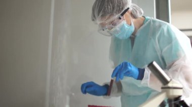 Koruyucu giysiler içindeki kadın bir teknik teknisyen Coronavirus Covid-19 'a bulaşmış kan örnekleriyle çalışıyor. Covid-19 virüsünün bilimsel araştırması.