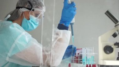 Mikrobiyolog laboratuvarda Coronavirus Covid-19 virüsü bulaşmış kan örnekleri üzerinde çalışıyor. Koruyucu kıyafetli bir laboratuvar asistanının elinde boru dağıtıcı.