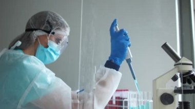 Koruyucu kıyafetli bir laboratuvar asistanının elindeki boru pompası. Mikrobiyolog laboratuvarda Coronavirus Covid-19 enfeksiyonlu reaktörler ve kan örnekleriyle çalışıyor.