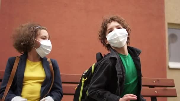 Cute curly boy and girl are sitting on a bench at a safe distance and talking. Back to school after quarantine — Stock Video