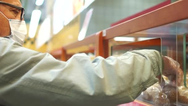 Gemaskerde man met handschoenen kiest een broodje in de bakkerij van een groot winkelcentrum. Regels voor het bezoeken van supermarkten na quarantainedoeleinden — Stockvideo