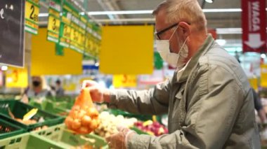 Gri saçlı, yaşlı bir adam süpermarkette soğan alıyor. Karantina Coronavirus Covid-19 sırasında alışveriş.