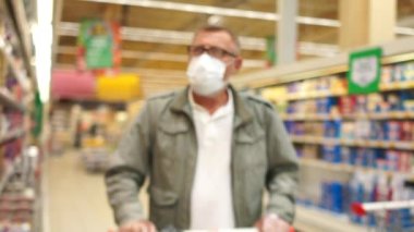 Karantina bittikten sonra süpermarketleri ziyaret etme kuralları. Maskeli ve eldivenli gri sakallı emekli büyük bir mağazanın rafları arasında el arabası taşıyor.