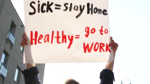 Malato - stare a casa sano - andare al lavoro. Una donna con una maschera tiene un poster in testa con l'iscrizione. Mantenere la distanza protesta sociale — Video Stock