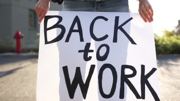 Крупный план неопознанной женщины, держащей плакат у своих ног с надписью "Назад к работе". Массовые протесты против ограничительных мер во время карантинной изоляции коронавируса ковид-19 — стоковое видео