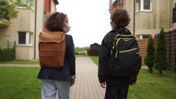 Adolescentes rizados, un niño y una niña van a la escuela con máscaras protectoras. De vuelta a la escuela después de la cuarentena, terminando el bloqueo. Vista trasera. Vida post-cuarentena — Vídeo de stock