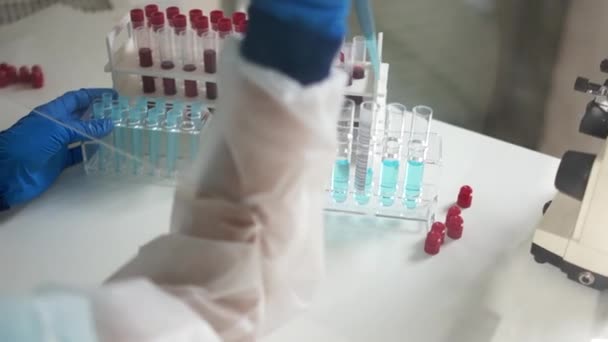Närbild av en laboratorieassistent hand av en kvinna i skyddsdräkt gör forskning med blodprov av ett virus infekterat. Diagnos av coronavirus covid-19 i laboratoriet — Stockvideo