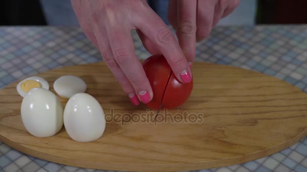 Detail z rukou mladé dívky s kuchyňským nožem řezat zralé rajče na polovinu, pak dal dvě poloviny vedle rajčat na kuchyňské desce